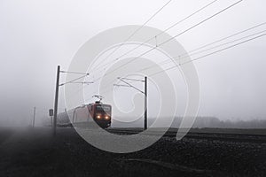 Red train locomotive  through mist moving on railway tracks
