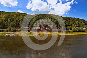 Red train at the Railway station on picturesque bank of the Elbe River of the Elbe river. Small white ferryboat