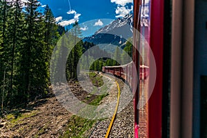 Red train slowly climbing to the Bernina Pass in the Swiss Alps
