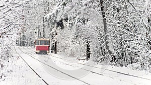 Red tram moving on the rails in the winter snowy forest