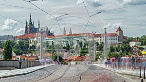 Red tram passing on Manes Bridge timelapse and famous Prague Castle on the background in Prague, Czech Republic.