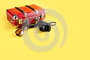 Red travel suitcase, sunglasses and a camera on a yellow background. Travel concept. Place for your text.