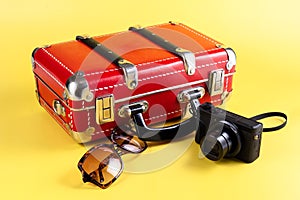 Red travel suitcase, sunglasses and a camera on a yellow background. Travel concept. Place for your text.