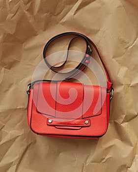 Red trendy luxury texture leather handbag with a long strap on a wrinkled craft brown paper background