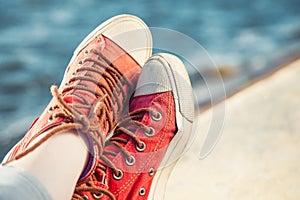 Red trendy sneakers on girl and seascape as background