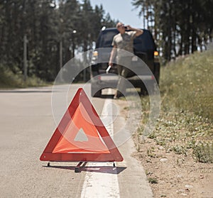 Red triangle caution sign on road after car break down and blurred driver speaking on cellphone, calling emergency