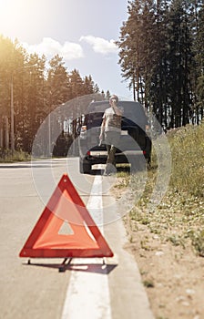 Red triangle caution sign on road after car break down and blurred driver speaking on cellphone, calling emergency