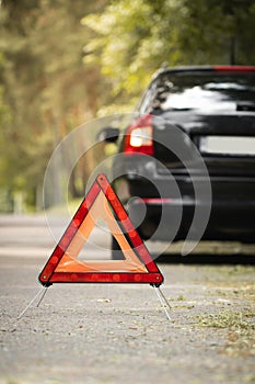 Red triangle, red emergency stop sign and black car with technical problems in the blurred background. Emergency stop of the car