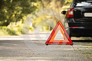 Red triangle, red emergency stop sign and black car with technical problems in the blurred background. Emergency stop of the car