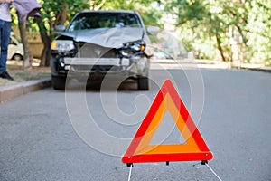 Red triangle warning sign of car accident on road. Triangle in front of wrecked car in summer time.