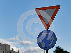 A red triangle yield or give way roundabout sign attached on a pole against a blue sky