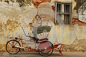 Red trishaw in front of weathered wall photo