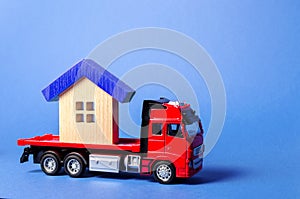 Red truck carrier transports a blue roofed house. Concept of transportation and cargo shipping, moving company