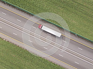 Red truck driving on asphalt road along the green fields. seen from the air. Aerial