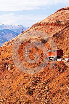 Red truck driving on a mountain road on winter dusk, fantastic landscape of red mountain ridge and snow mountains backdrop