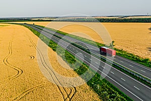 Red truck on the higthway among the wheat fields. cargo delivery driving on asphalt road