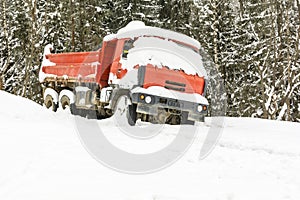 A red truck left in the winter near the forest