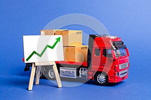 Red truck loaded with boxes and stand with a green up arrow. Raise economic indicators and sales. Exports, imports. High trade photo