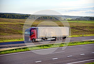Red truck with semi-trailer driving along highway on the sunset background. Goods delivery by roads. Services and Transport