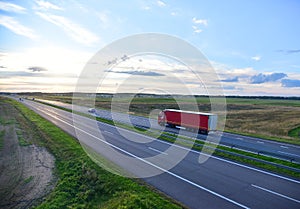 Red truck with semi-trailer driving along highway on the sunset background. Goods delivery by roads. Services and Transport