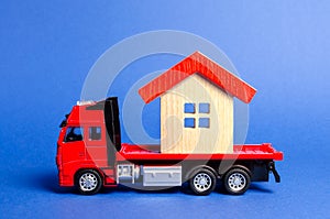 Red truck transports a red roofed house. Concept of transportation and cargo shipping, moving company. Construction of new houses