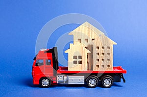 Red truck transports wooden houses. Concept of transportation and cargo shipping, moving company. Construction of new houses