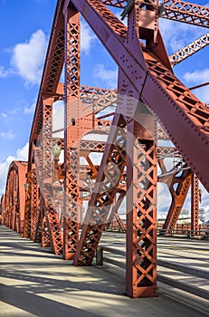 Red trusses constructing a Broadway drawbridge over the Willamette River in Portland with long shadows from bright sunlight