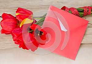 Red tulips bouquet with white paper card & envelope on wooden ta