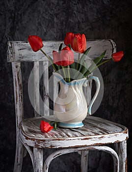 Red tulips bouquet in white vase on vintage cher.