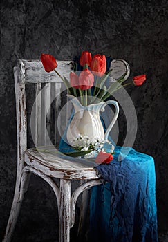 Red tulips bouquet in white vase on vintage cher.