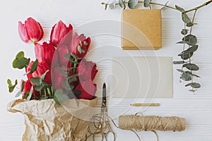 Red tulips with greeting card, gift, pencil, scissors and twine on rustic white wood flat lay