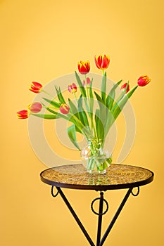Red tulips in a vase on mosaic table.