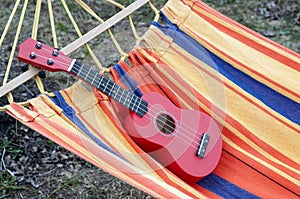 Red ukulele left in a colorful hammock. Musical instrument.