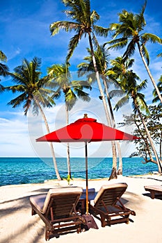 Red umbrella and chairs on sand beach in tropic photo