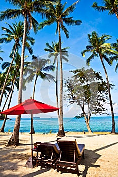 Red umbrella and chairs on sand beach in tropic