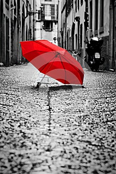 Red umbrella on cobblestone street in the old town. Wind and rain