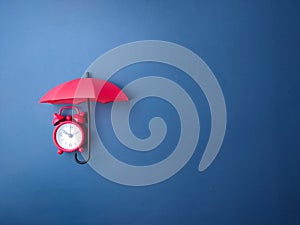 Red umbrella and red alarm clock on a blue background