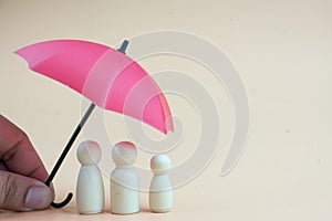 Red umbrella with wooden family peg dolls for protection with copy space. Family protection and insurance coverage concept