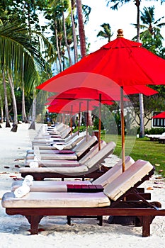 Red umbrellas and chairs on sand beach in tropic