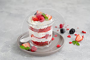 Red Velvet cake trifle with fresh berries in a glass jar on a gray concrete background. Dessert for Valentine`s Day. Copy space