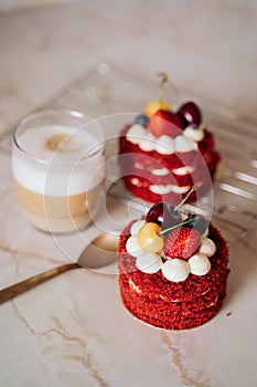 Red velvet cakes, portioned, decorated with cherries and strawberries. transparent mug of cappuccino with a cinnamon stick. delici