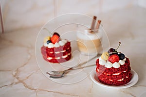 red velvet cakes, portioned, decorated with cherries and strawberries. transparent mug of cappuccino with a cinnamon stick. delici