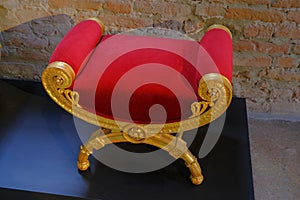 Red velvet chair with golden decor on the floor across brick wall. Interior design. Home furniture