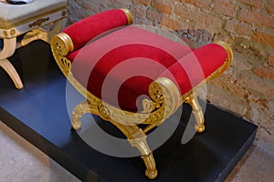 Red velvet chair with golden decor on the floor across chairs and brickwall. Interior design. Home decor.