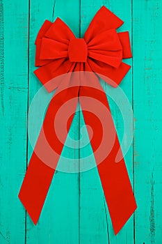 Red velvet Christmas bow and ribbon hanging on antique teal blue rustic wooden background