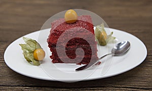 Red Velvet, fresh delicious diet cake with berry Physalis at Dukan Diet on a porcelain plate with a spoon on a wooden background