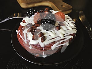 Red velvet pancakes served with melted white chocolate sauce and raspberries, blackberries and pomegranate seeds