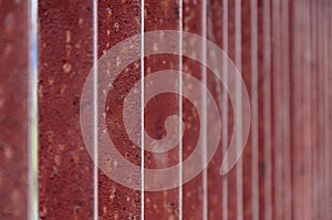 red vertical lines. Old rusty metal fence. Red background. Soft focus at the edges from the center of the frame. Background for