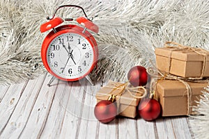 Red vintage alarm clock and three gift boxes on a wooden table decorated with a garland and red Christmas balls for the New Year