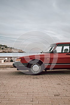 Red vintage car from the 90s with view of tropical sea and white houses on a hill where you can see the nose clear